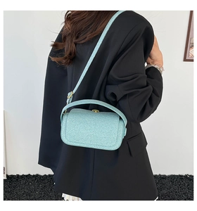Detail of light blue glitter crossbody bag with gold hardware against a black blazer