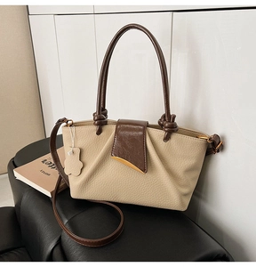 Detail of two-tone beige leather handbag with brown flap and gold crescent buckle hardware