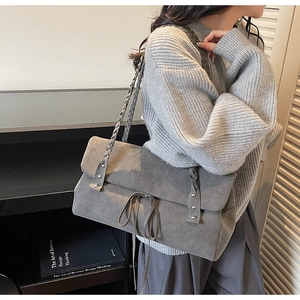 Detail of grey suede shoulder bag featuring a braided strap and minimalist rivet accents