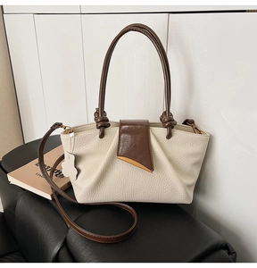 Close-up of pleated beige tote bag featuring contrast brown handles and gold triangle metal buckle