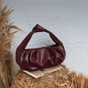Deep red pleated cloud bag with knotted handle displayed on a rustic decor setting