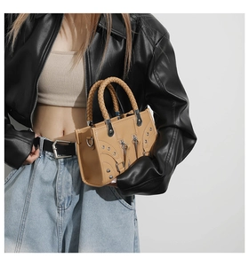 Detail of tan tote bag with metal zippers, silver studs, and woven leather handles