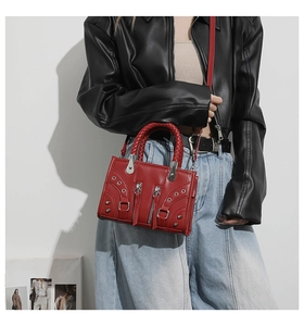Detailed view of red leather crossbody bag with silver studs and braided handle texture