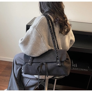 Dettaglio di una borsa tote in pelle scamosciata nera con spallacci intrecciati e borchie in metallo