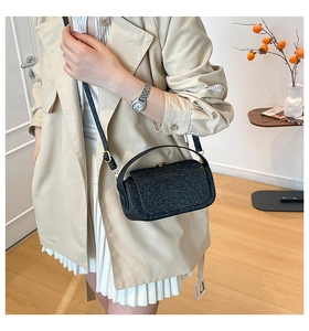 Detail of a chic black glitter crossbody box bag with gold metal hardware on a female model