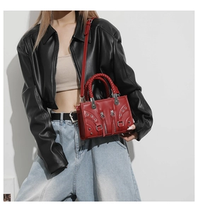 Detail of red punk style leather handbag with metal rivets and woven handles on a model