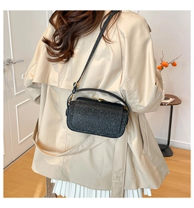 Close-up of black sequin crossbody bag with gold hardware worn on a beige trench coat