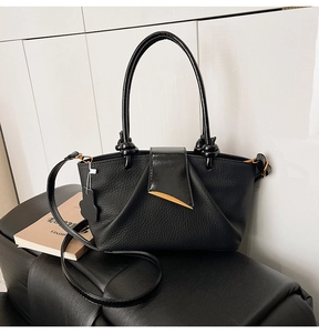 Close-up of black leather handbag with knotted handle and golden leaf buckle detail