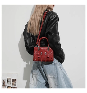 Detail of red punk style crossbody bag with silver eyelets and braided handle