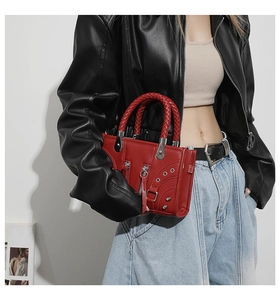 Detail of red punk-style tote bag with decorative zippers, rivets, and woven handle