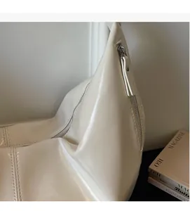 Detailed close-up of the zipper and stitching on the beige glossy leather dumpling bag