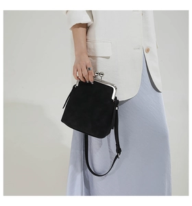 Detailed view of black kiss-lock bag with matte suede texture and silver metal clasp