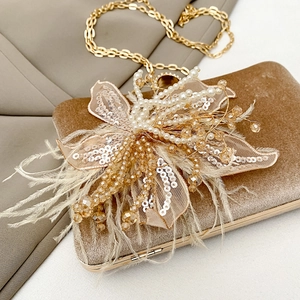 Close-up of champagne velvet evening clutch with 3D floral pearls and feather detail