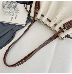 Detailed view of cream pebble leather bucket bag with brown drawstrings and silver buckle