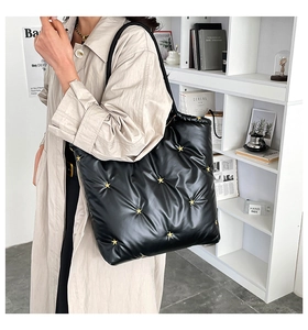 Detail of black quilted tote bag with gold star rivets shown on shoulder style