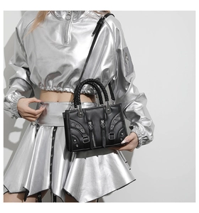 Detail of a black punk-style leather bag with metal eyelets and woven handles on a model