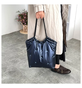 Detail of navy blue quilted tote bag with star embroidery held by a woman in a trench coat