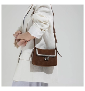 Brown vintage suede crossbody bag with metal sphere clasp shown on a white blazer