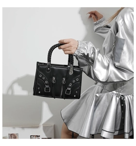 Detail of black motorcycle style handbag featuring woven handles and metallic rivets