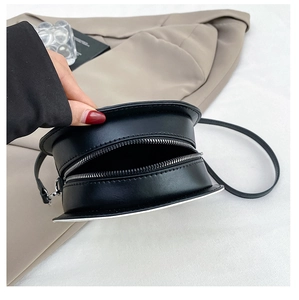 Detailed side view of black leather round crossbody bag showing zipper closure and texture