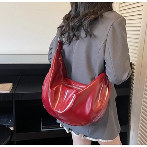 Detail of red glossy crescent shoulder bag showing premium leather texture and zipper