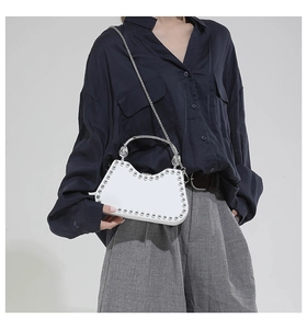 Detail of white leather half-moon bag featuring silver rivet studs and ring handle