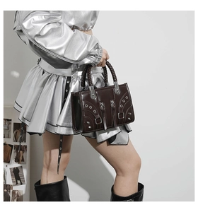 Detail of dark brown leather handbag with silver studs and woven handle on model
