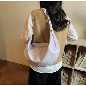 Detail view of a light purple glossy crescent hobo bag worn by a model in a cozy room