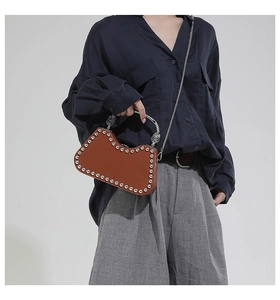 Detailed side view of brown leather bag with silver rivets and metal U-shaped handle