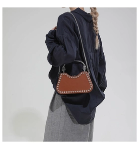 Detail of a brown leather box bag with silver studs and chain strap on a model