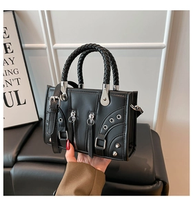 Detail of black faux leather handbag featuring woven handles and silver metallic hardware