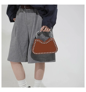 Detail of a brown leather box bag featuring silver rivets and a twisted metal handle