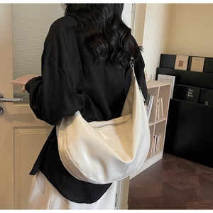 Detail of a cream faux leather crescent bag featuring a wide strap and glossy finish