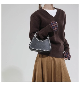 Detail of black leather handbag featuring silver studs and metal handle on model