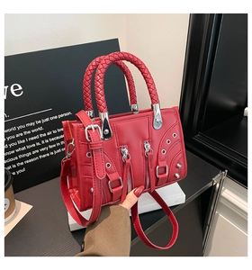 Detail of red rivet handbag with woven handles and metal zippers in a cafe setting