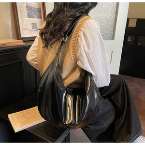 Detail of a large black crescent shoulder bag with glossy texture and metal buckle