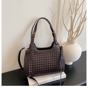 Détail du sac à main tissé marron foncé avec accents dorés posé sur des livres
