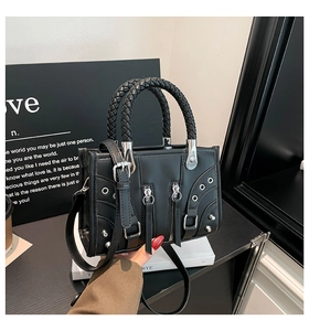 Detail of black faux leather handbag featuring woven handles and metal rivet hardware