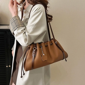 Brown bucket shoulder bag with drawstring pleats worn with a trench coat