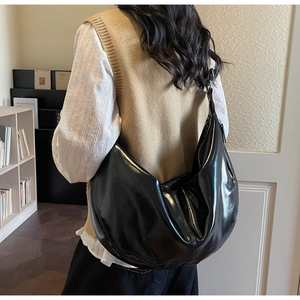 Side view of a large black patent leather hobo bag worn by a model in a minimal setting