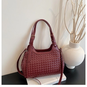 Détail macro de la texture en cuir tressé bordeaux et structure trapèze du sac de luxe