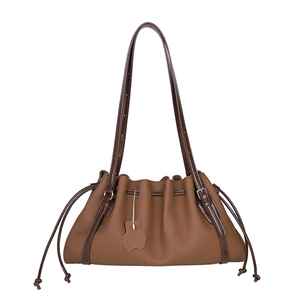 Large tan leather drawstring bucket bag with a floral charm and dark brown shoulder strap