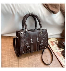 Detail of dark brown leather handbag with braided handle, silver studs and zippers