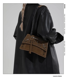 Close-up of brown suede shoulder bag with metal chains and rivets on a black coat