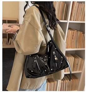 Nahaufnahme einer glänzenden schwarzen Hobo-Tasche mit Nieten und Metallplakette