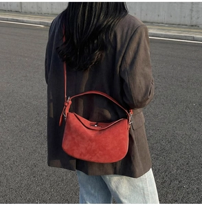 Street style shot of red suede dumpling bag featuring adjustable strap and silver metal buckle