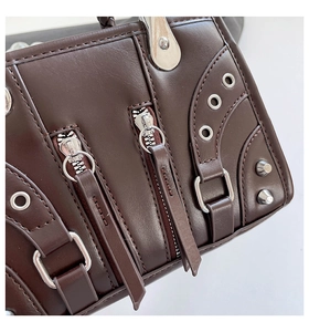 Close-up of dark brown leather motorcycle bag with silver zippers and stud details