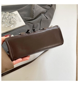 Detail view of dark brown leather handbag base featuring silver metal rivets and buckle