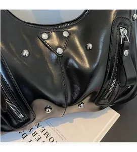 Detail der schwarzen glänzenden Ledertasche mit silbernen Nieten und ikonischer Metallplakette