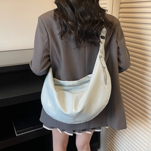 Glossy light blue crescent shoulder bag with wide strap worn by model in a street style view